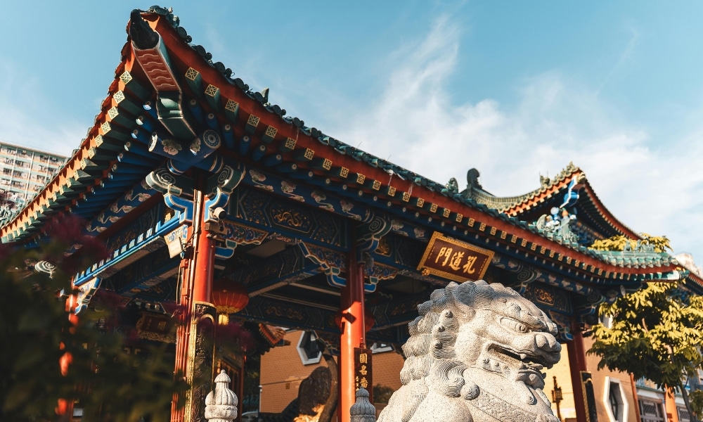 ประตูวัดจีนแบบดั้งเดิมที่มีหลังคาประดับอย่างวิจิตร พร้อมรูปปั้นสิงโตหินตั้งอยู่ด้านหน้า ท่ามกลางท้องฟ้าสีคราม สถานที่สักการะเทพเจ้าต่างประเทศแห่งนี้มอบบรรยากาศอันเงียบสงบที่สะท้อนถึงมรดกทางจิตวิญญาณ.