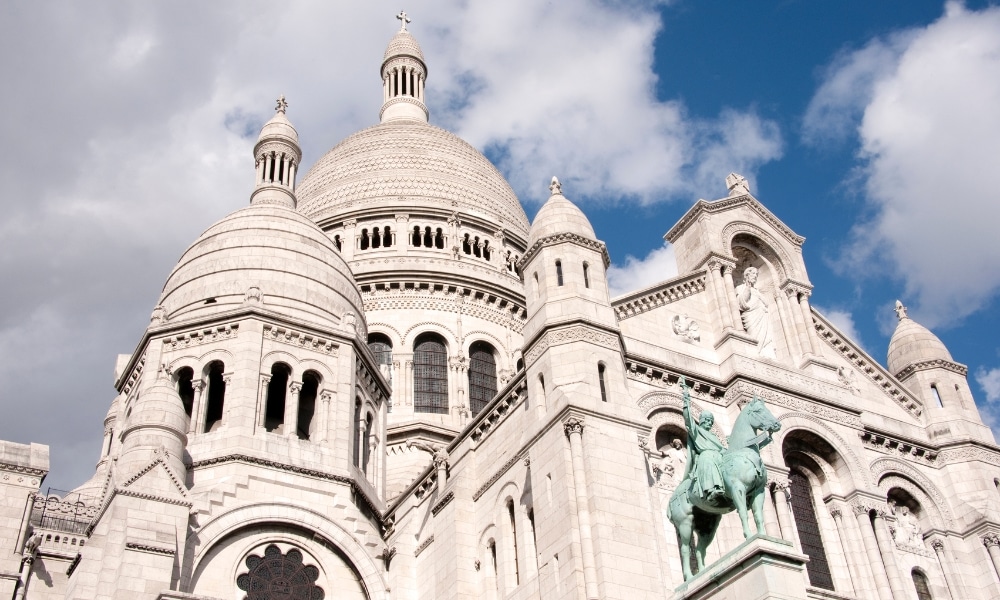 วิหารโดมสีขาวทรงกลมพร้อมรูปปั้นม้าและคนขี่ ตั้งอยู่เบื้องหลังท้องฟ้าสีฟ้าสดใสที่มีเมฆลอยอยู่—สถานที่ศักดิ์สิทธิ์ของเทพเจ้าต่างประเทศที่โดดเด่นซึ่งชวนให้รู้สึกทึ่งและชื่นชม.