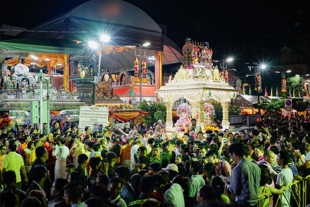 ฝูงชนจำนวนมากมารวมตัวกันในยามค่ำคืน ฉลองใกล้กับโครงสร้างทางศาสนาที่ประดับประดาอย่างวิจิตรและสว่างไสว พร้อมตั้งคำถามว่าฝันเห็นพญานาคสีอะไรจะนำโชค ท่ามกลางบรรยากาศแห่งเทศกาลอันคึกคัก.